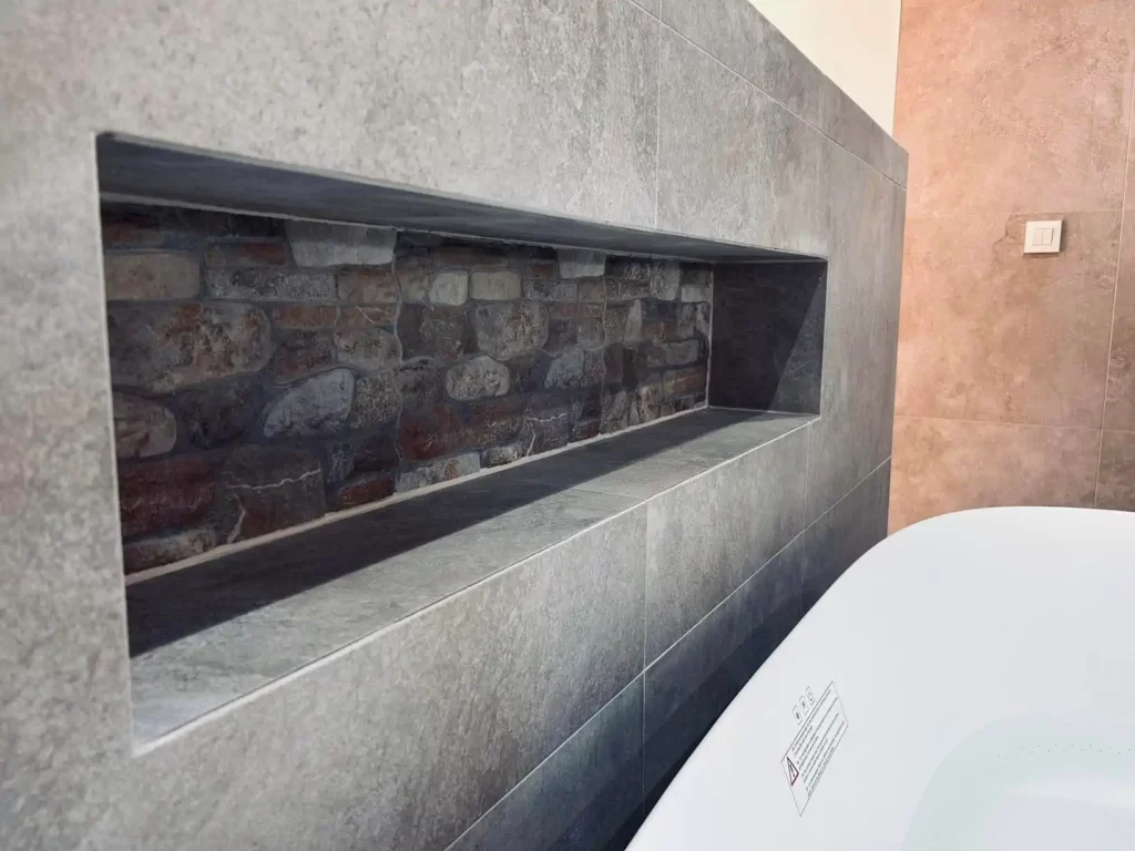 Détail d’une niche murale en pierre naturelle intégrée dans une salle de bain contemporaine rénovée à Baelen