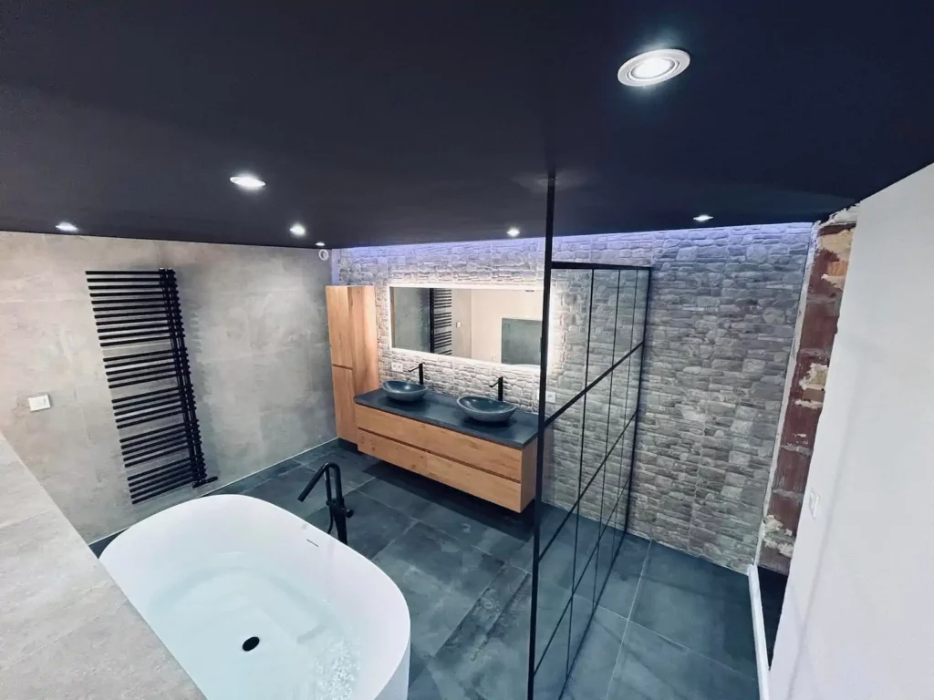 Salle de bain contemporaine rénovée à Baelen avec baignoire îlot, double vasque en bois et mur en pierre