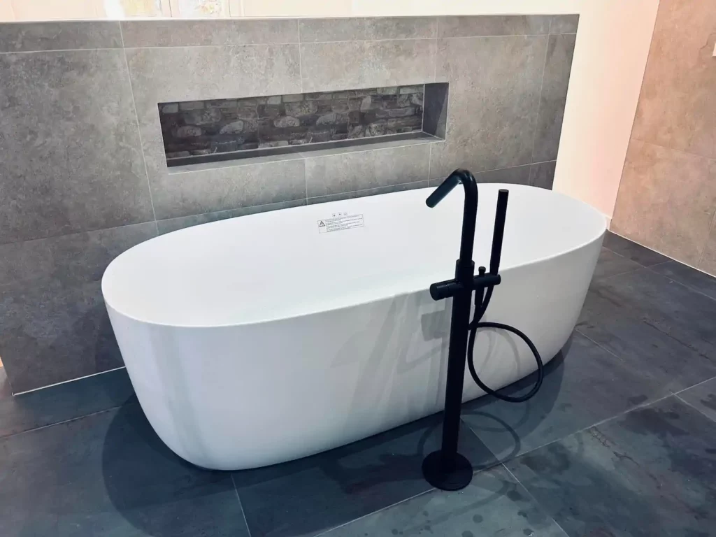 Salle de bain contemporaine rénovée à Baelen avec baignoire îlot blanche, robinetterie noire et niche murale