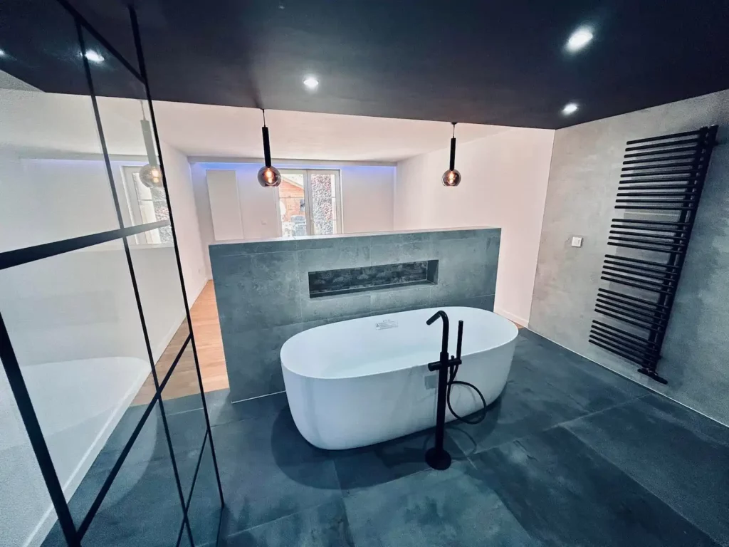 Salle de bain moderne rénovée à Baelen avec baignoire îlot, robinetterie noire et radiateur sèche-serviettes