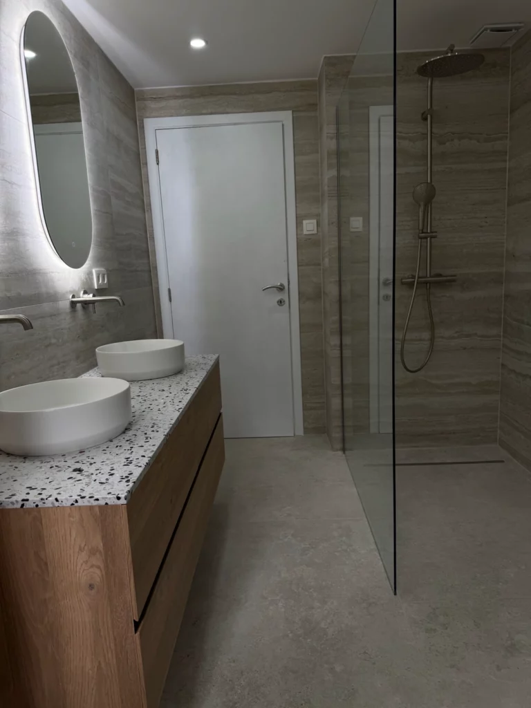 La salle de bain rénovée présente un meuble en bois avec deux vasques rondes sur un plan en terrazzo, un
