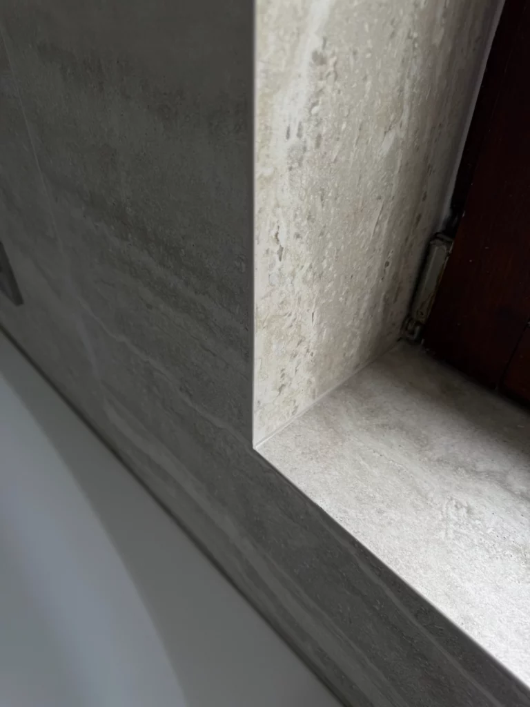Détail du rebord de fenêtre en pierre naturelle au-dessus de la baignoire, soulignant les finitions de la