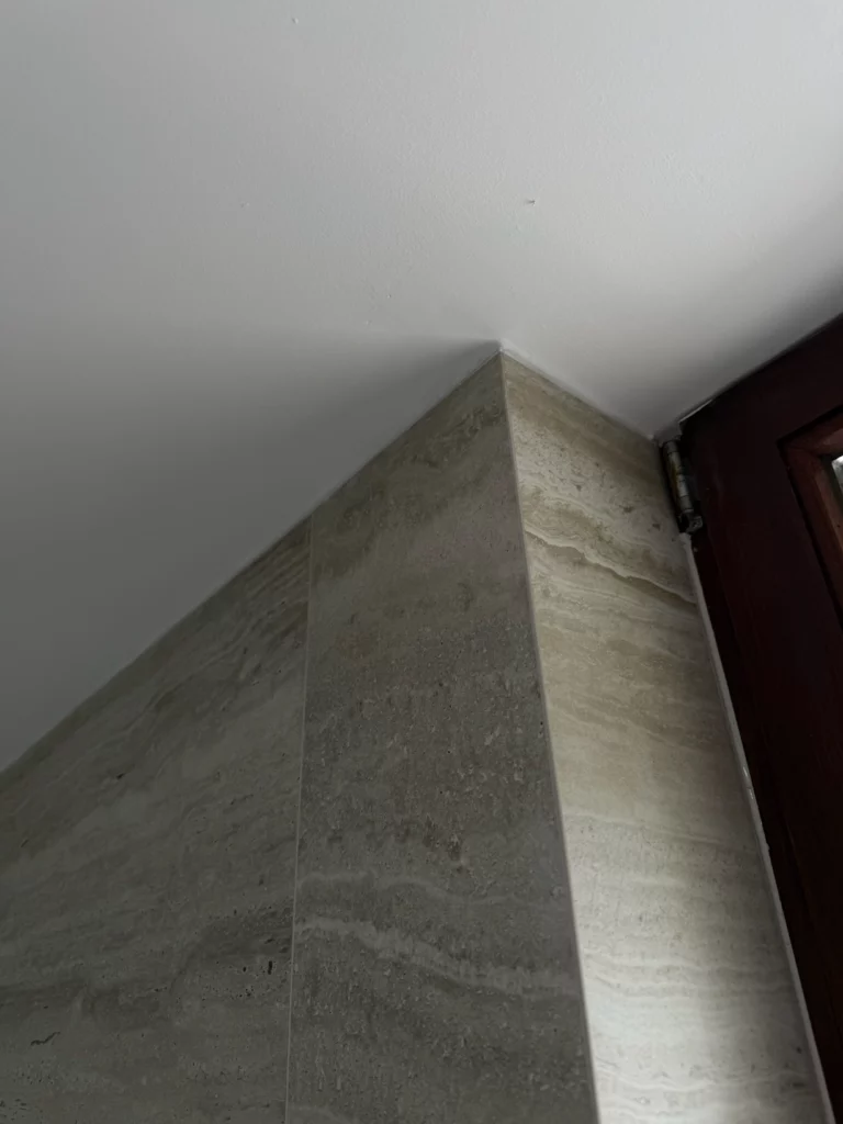 Détail de l'angle entre le mur en carrelage pierre naturelle et le plafond blanc dans la salle de bain