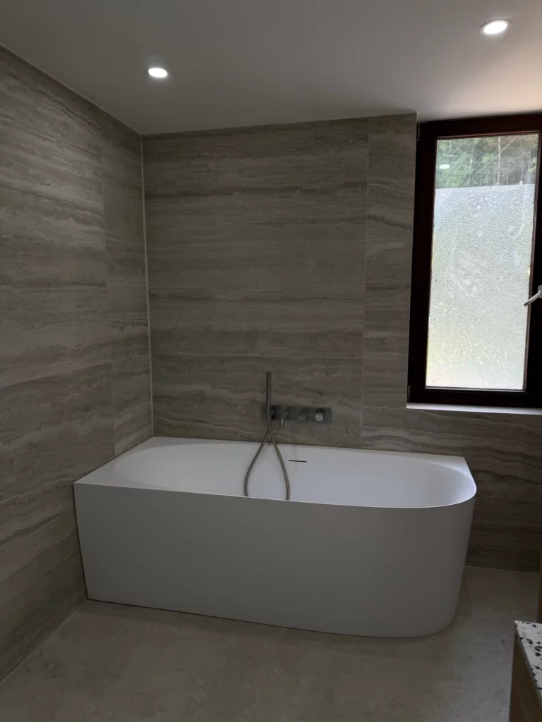 Vue d'ensemble de la salle de bain rénovée à Chaudfontaine : baignoire îlot ovale devant une fenêtre, murs en