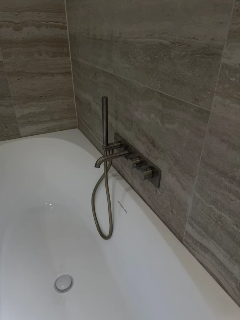 Baignoire encastrée avec robinet mural et douchette flexible sur fond de carrelage effet pierre, dans une