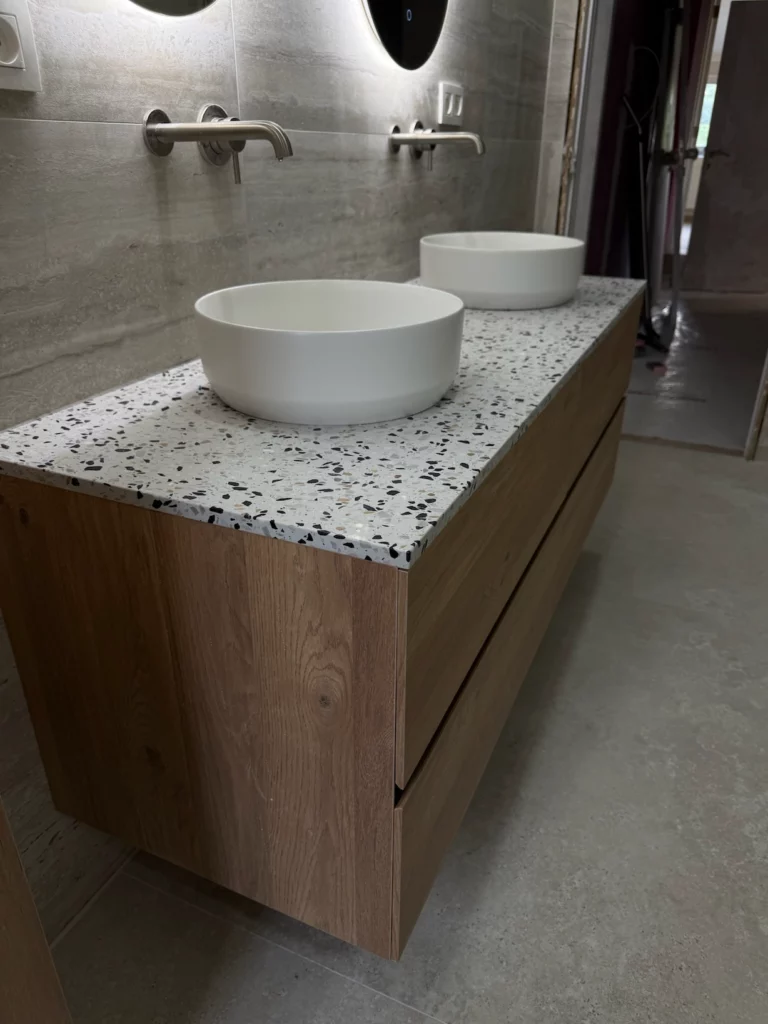 Vue du plan vasque en terrazzo avec deux vasques rondes et meuble en bois, robinetterie murale moderne, dans