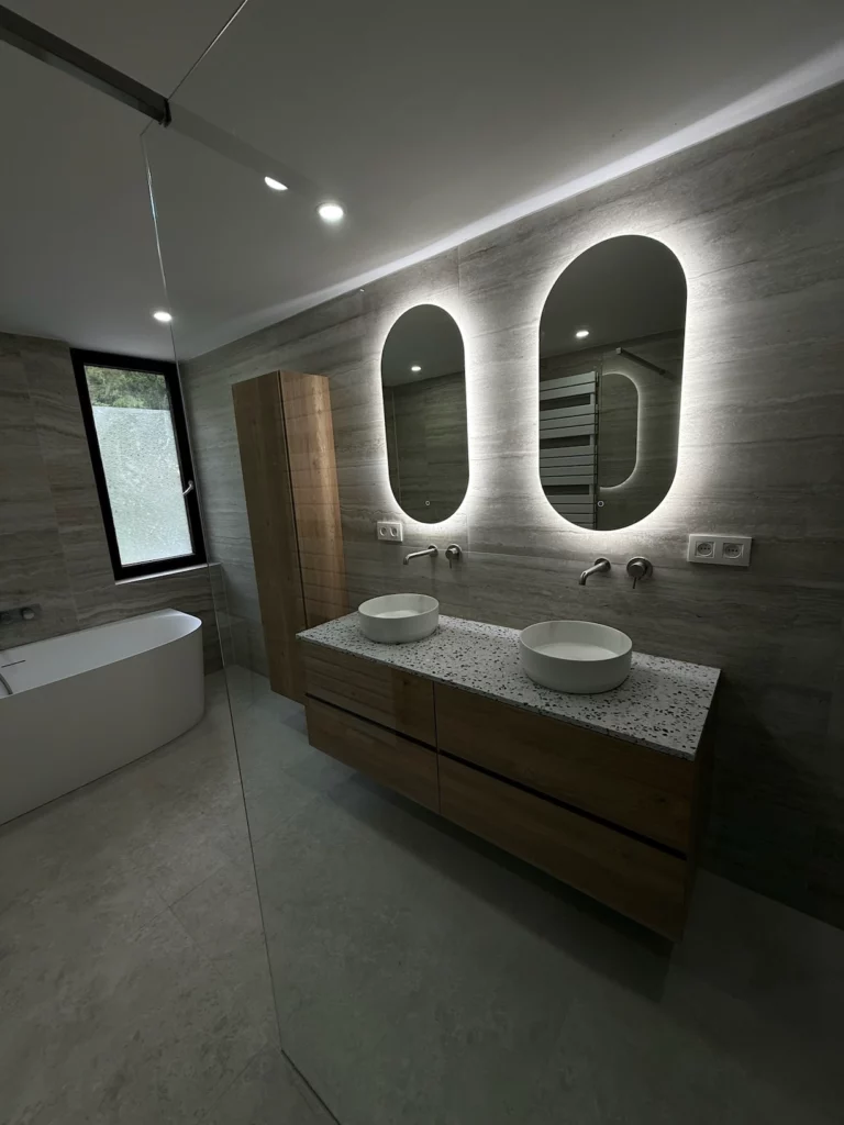 Vue de la salle de bain rénovée avec une baignoire îlot, un meuble vasque en bois sur plan terrazzo et deux
