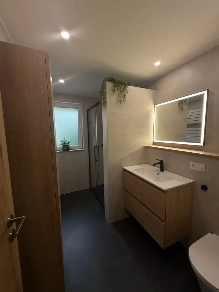 Vue d'ensemble de la salle de bain rénovée à Jalhay : meuble vasque suspendu en bois avec miroir