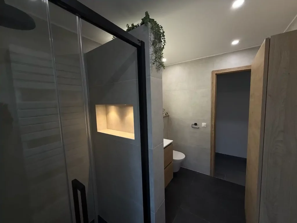Vue d'ensemble de la salle de bain rénovée à Jalhay : paroi de douche vitree avec cadre noir, niche murale