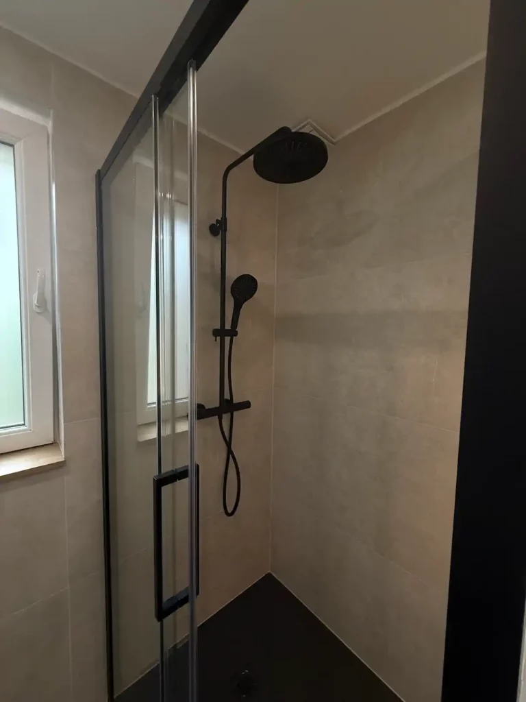 Douche à l'italienne avec paroi vitree pivotante et colonne de douche noire avec pommeau pluie et douchette,