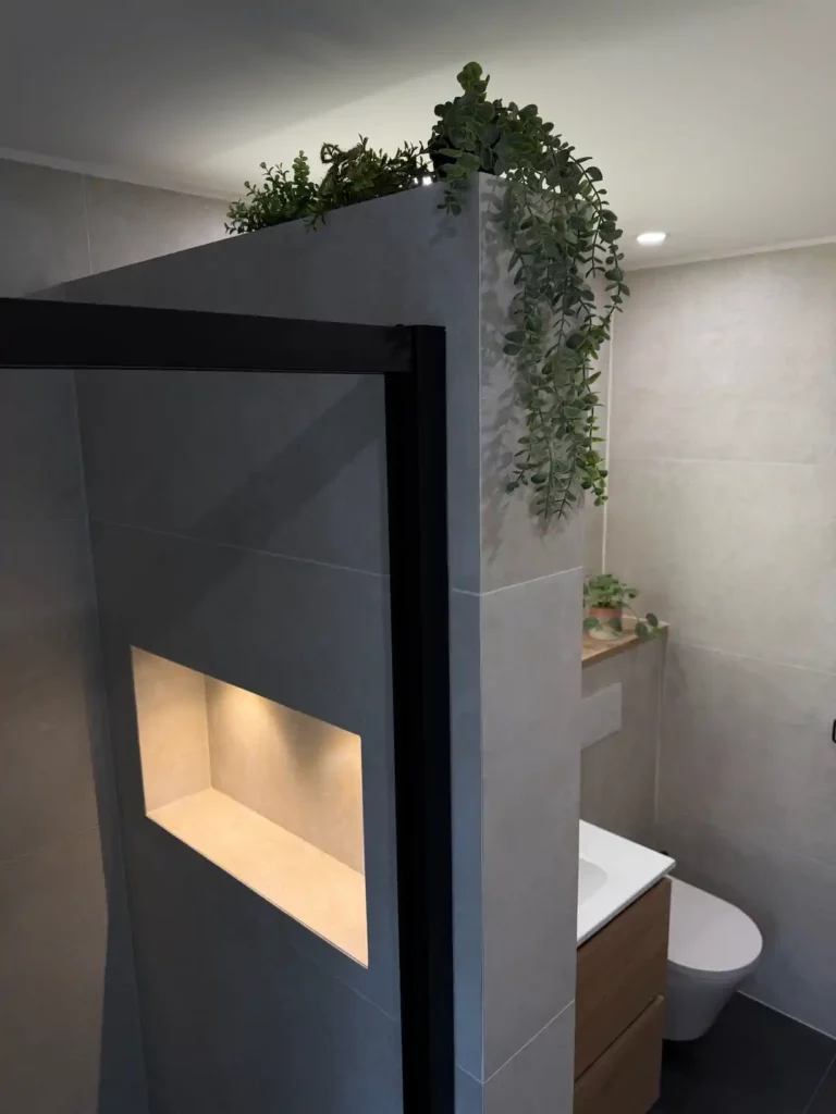 Zoom sur la cloison de douche en verre à cadre noir intégrant une niche murale éclairée, décorée de plantes,