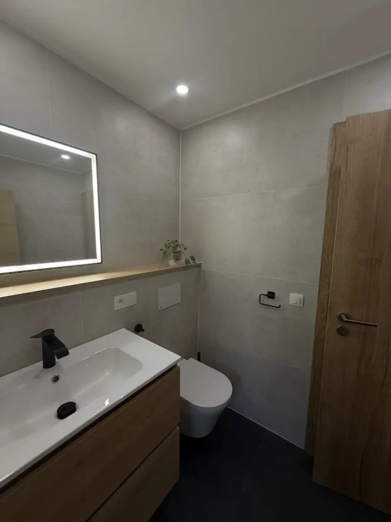 Vue latérale de la salle de bain rénovée à Jalhay : meuble vasque en bois avec robinet noir et vasque