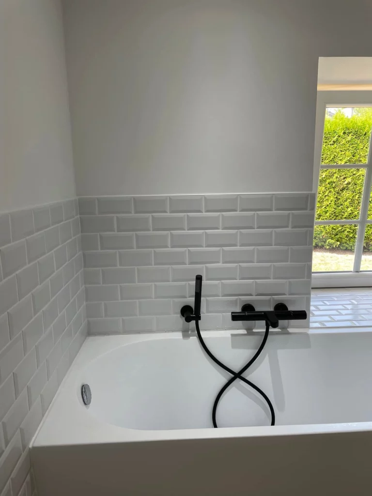 Détail d’une baignoire encastrée avec robinetterie noire et carrelage métro, rénovation à Saint-Vith