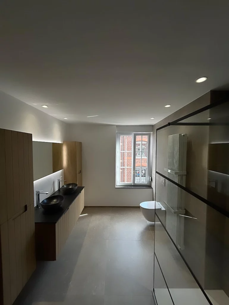 Vue d’ensemble d’une salle de bain contemporaine rénovée à Welkenraedt, avec double vasque, douche vitrée et