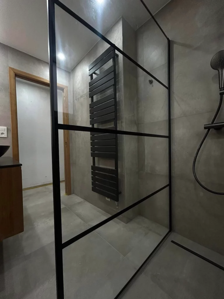 Vue intérieure de la douche avec paroi verrière noire et sèche-serviettes design dans une salle de bain