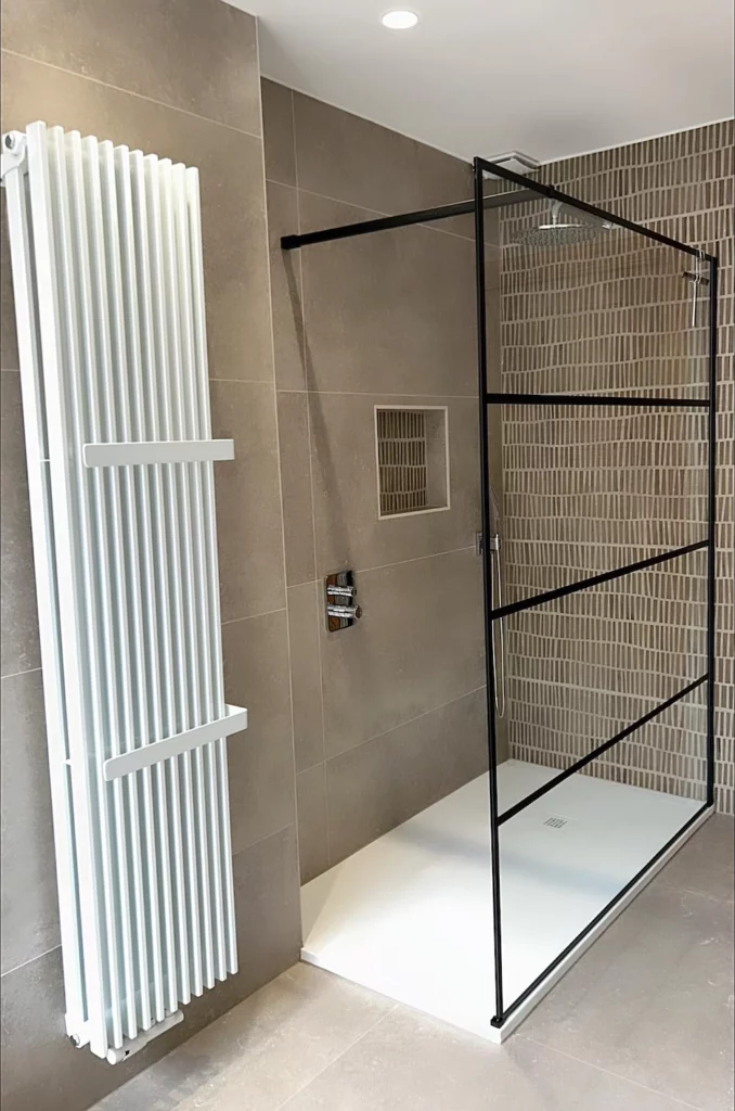 Douche à l’italienne avec paroi vitrée à structure noire et radiateur sèche-serviettes dans une salle de bain