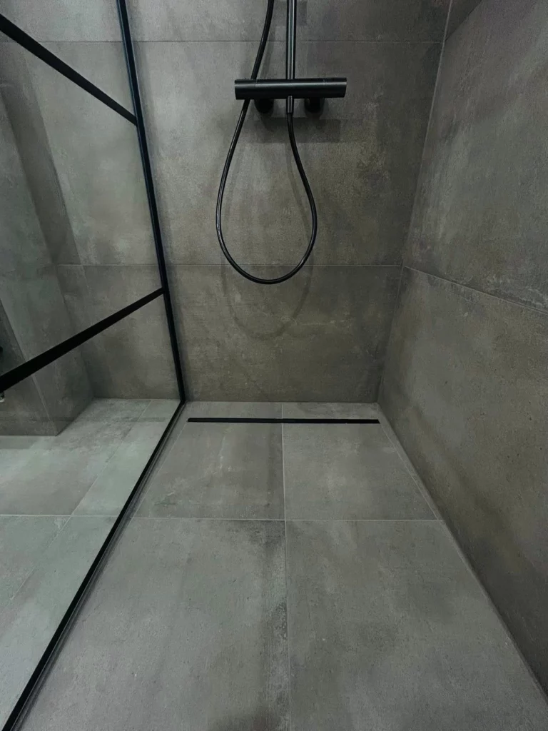 Détail de la douche avec paroi verrière noire et finitions contemporaines, rénovation réalisée à Welkenraedt