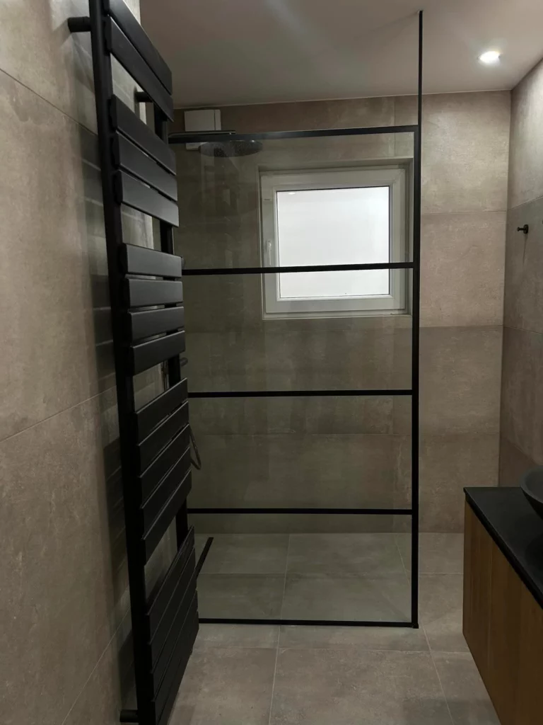 Douche à l’italienne moderne avec paroi vitrée noire et carrelage effet béton, rénovée à Welkenraedt